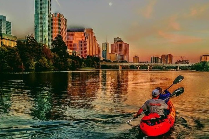 people kayaking in city lake during sunset